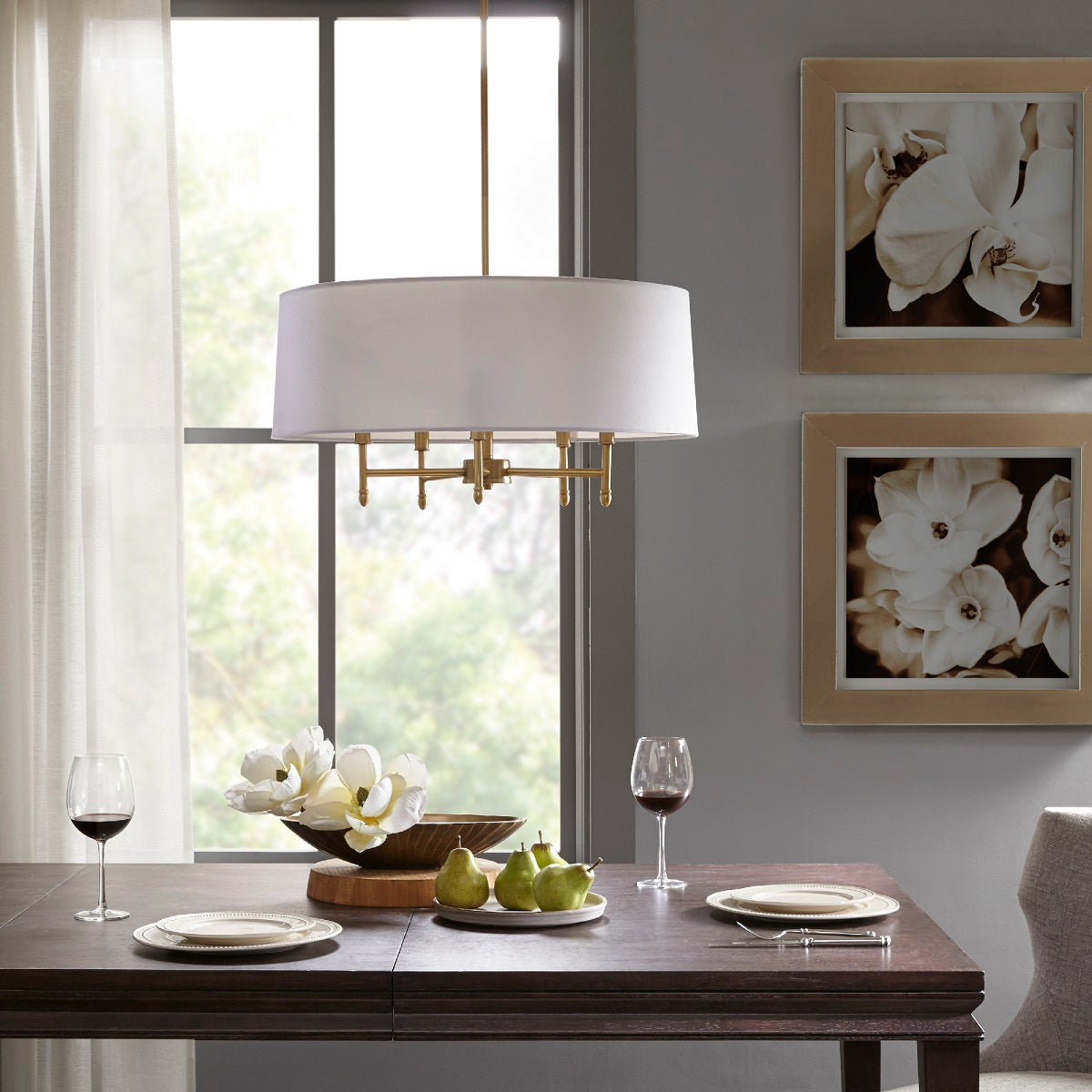 5-light chandelier with white drum shade and brass frame above a dining table